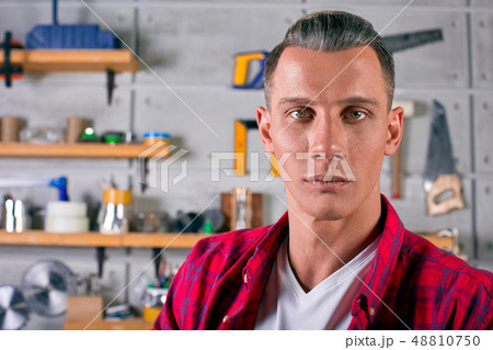 locksmith stands in the workshop on the background of the wall with shelves under the tools locksmith stands in the workshop on the background of the wall with shelves under the tools 48810750