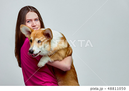 Beautiful girl with a Welsh Corgi on her hands on a gray background, copy space 48811050