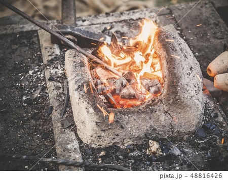 The blacksmith holds the billet over hot coals in a clay oven. blacksmith heating iron metal sword 48816426