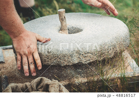 The ancient quern stone hand mill with grain. The man grinds the grain into flour with the help of a 48816517
