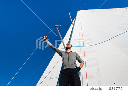 Yacht captain with a beard stands on sail boom on a sailing yacht, holding the rope in his hand and Yacht captain with a beard stands on sail boom on a sailing yacht, holding the rope in his hand and 48817794