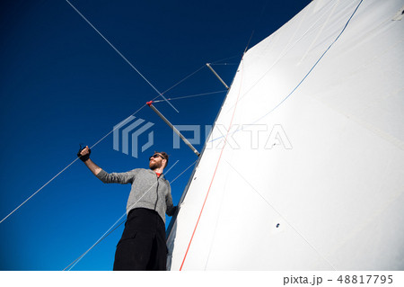 Young man lifting the sail of catamaran during cruising Young man lifting the sail of catamaran during cruising 48817795