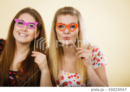 Two happy women holding fake eyeglasses on stick 48829947