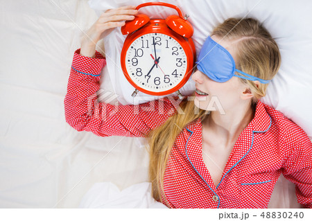 Sleeping woman wearing pajamas holding clock 48830240