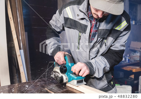 A young carpenter with a beard works with an electric plane without suctioning sawdust. Leveling and 48832280