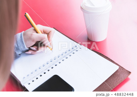 Close-up from behind the back of a young woman in a winter polto is holding a ballpoint pen and is 48832448