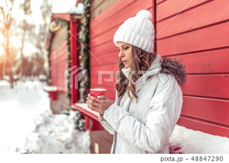 A beautiful girl in the winter in city near the red shutters, a cup of coffee is warming and blowing 48847290