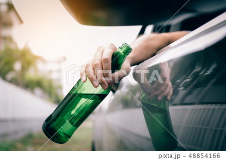 Asian man holding a bottle of beer outside the car Asian man holding a bottle of beer outside the car 48854166