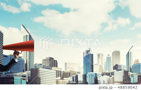 Hand of businesswoman holding red paper trumpet against cityscape background 48859042