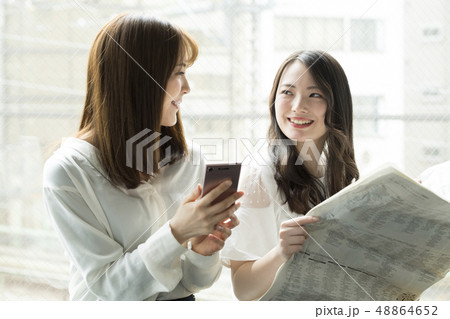 窓辺でスマホと新聞を見る女性二人 窓辺でスマホと新聞を見る女性二人 48864652
