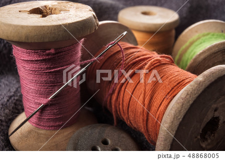 Sewing needle and cotton thread on wooden spool macro view. 48868005