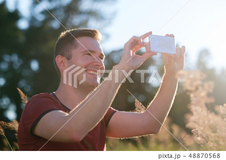 Young man holding mobile phone in hands at sunset making a photo of nature on phone. 48870568