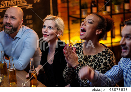 Group of friends watching tv in a cafe behind bar counter Group of friends watching tv in a cafe behind bar counter 48873633