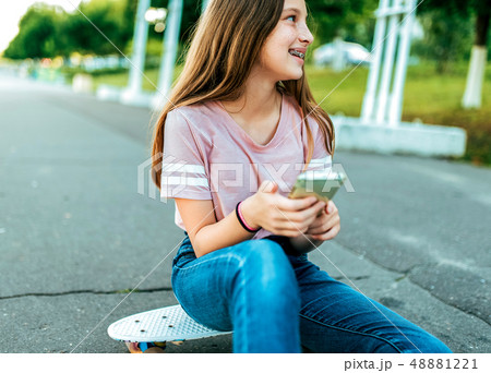 A little girl schoolgirl of 12-16 years old, on street she sits on a skateboard in summer in park A little girl schoolgirl of 12-16 years old, on street she sits on a skateboard in summer in park 48881221