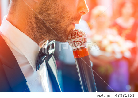 Profile of a handsome man with a microphone in his hands on a blurred background with guests. He is Profile of a handsome man with a microphone in his hands on a blurred background with guests. He is 48881351