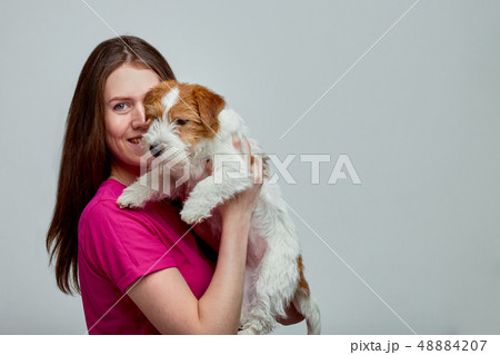 Beautiful girl with a jack russell terrier on her hands on a gray background, copy space 48884207