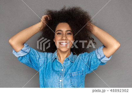 Freestyle. Mulatto woman standing isolated on grey touching hair laughing cheerful close-up 48892302