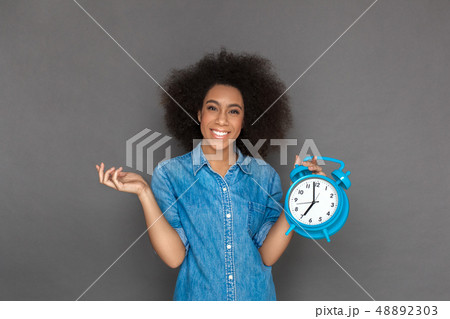 Freestyle. Mulatto woman standing isolated on grey with alarm clock smiling happy Freestyle. Mulatto woman standing isolated on grey with alarm clock smiling happy 48892303