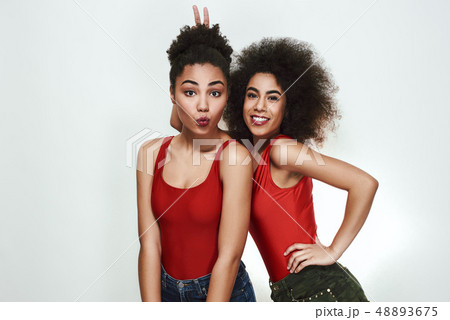 Happy moments. Two cute afro american women in jeans shorts are gesturing and making a face while 48893675