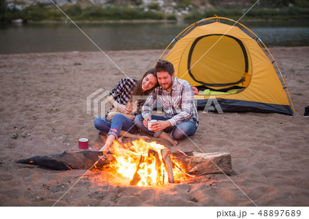 People, tourism and nature concept - Romantic evening, man embrace woman sitting near a campfire 48897689