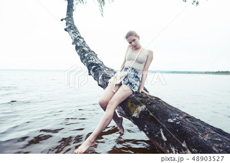 young blond woman hanging on birch tree at lake shore, summer vacations outdoor lifestyle 48903527
