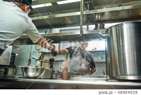 Take it. Young professional chef in apron giving a pepper grinder to his assistant while cooking 48904039