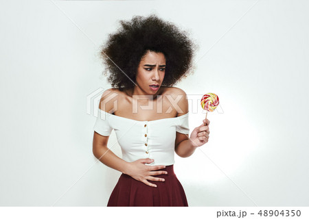 Don't eat sweets too much! Young afro american woman with colorful lollipop in hand got stomach ache Don't eat sweets too much! Young afro american woman with colorful lollipop in hand got stomach ache 48904350