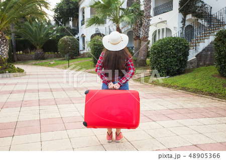 Travel, tourism and people concept - Back view of woman in hat carry a big red suitcase Travel, tourism and people concept - Back view of woman in hat carry a big red suitcase 48905366