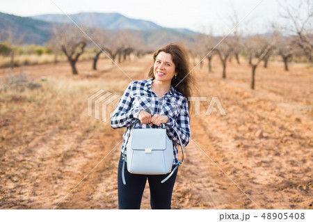 Trip, fashion and people concept - happy young woman walking with small bag and smiling over the Trip, fashion and people concept - happy young woman walking with small bag and smiling over the 48905408