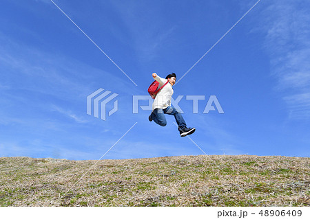 青空でジャンプする小学生の女の子 ランドセル の写真素材