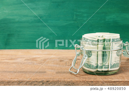 Dollar bills in glass jar on wooden table. Dollar bills in glass jar on wooden table. 48920850