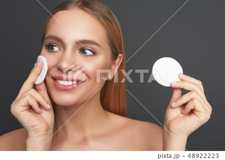 Pleased woman looking away while holding two cotton pads Pleased woman looking away while holding two cotton pads 48922223