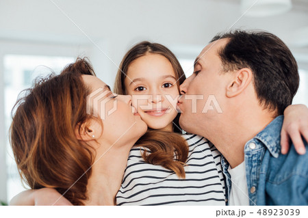 Happy parents kissing their daughter on cheek 48923039
