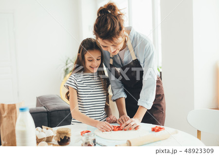 Happy girl smiling while making cookies with mother Happy girl smiling while making cookies with mother 48923309