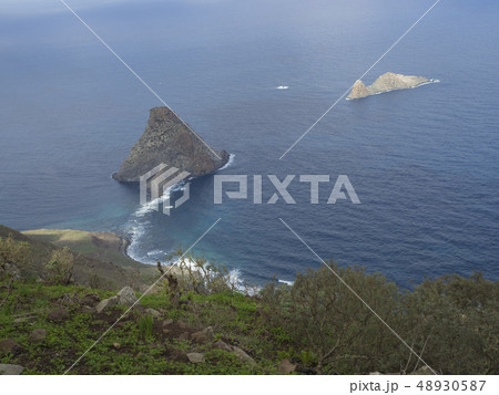 view on rock in the sea El Draguillo with green hills and dramatic blue sky white clouds in anaga 48930587