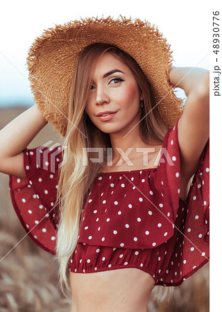 Portrait of a beautiful girl in a red dress and straw hat, in summer in the field. Long hair tanned 48930776