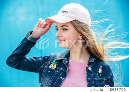 Portrait closeup beautiful smiling teenager girl in hat and denim jacket over blue wall Portrait closeup beautiful smiling teenager girl in hat and denim jacket over blue wall 48933706