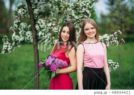 Two sisters walking outside in spring park. They hold a bouqet of lilac and smile Two sisters walking outside in spring park. They hold a bouqet of lilac and smile 48934421