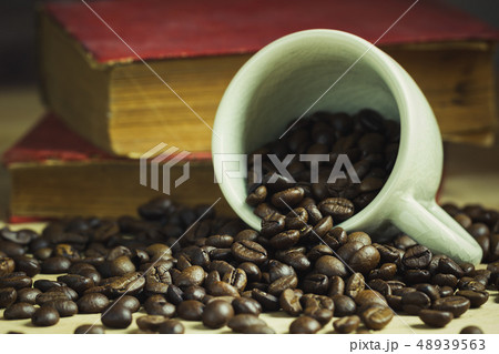 Coffee bean in tilted ceramic cup and old book. Coffee bean in tilted ceramic cup and old book. 48939563