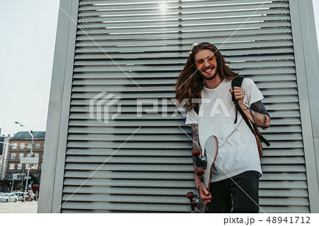 Cheerful hipster guy with tattoos on his hands holding skateboard 48941712