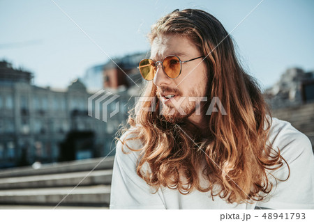 Handsome young man with long curly hair spending time outdoors Handsome young man with long curly hair spending time outdoors 48941793