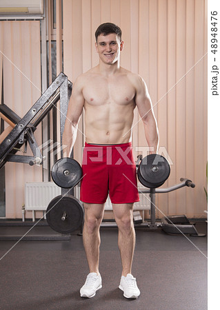 Young man flexing muscles with barbell in gym. Young man flexing muscles with barbell in gym. 48948476