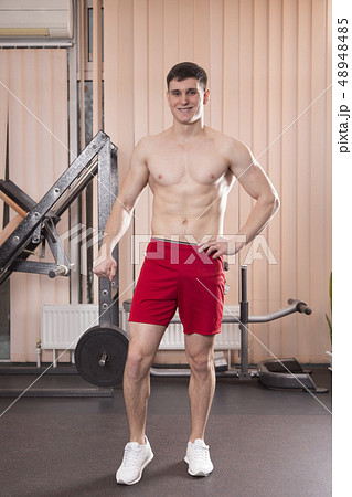 Young man flexing muscles with barbell in gym. Young man flexing muscles with barbell in gym. 48948485