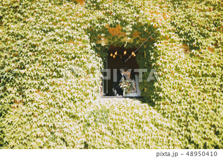 Stylish couple of happy newlyweds walking in the park on their wedding day with bouquet 48950410
