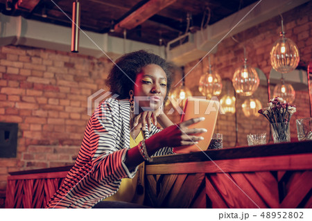 Concentrated Afro-American female watching video on tablet sitting at bar Concentrated Afro-American female watching video on tablet sitting at bar 48952802