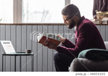 Man sitting near coffee table and reading book about astrology of money Man sitting near coffee table and reading book about astrology of money 48954205
