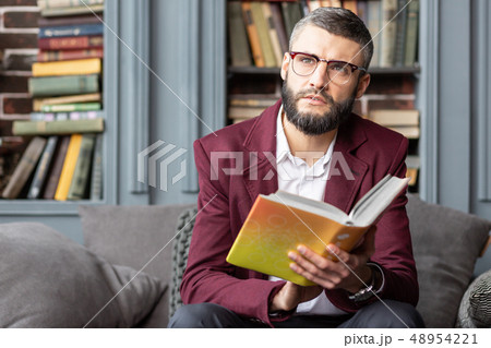 Dark-eyed bearded man feeling inspired after reading interesting book Dark-eyed bearded man feeling inspired after reading interesting book 48954221