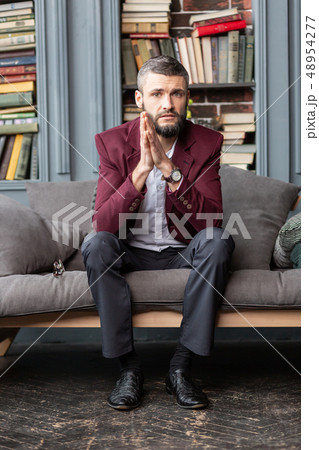 Handsome stylish businessman wearing dark red jacket sitting on sofa 48954277