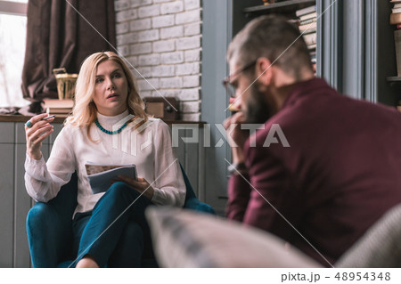 Blonde-haired psychologist wearing blue necklace listening to her client 48954348