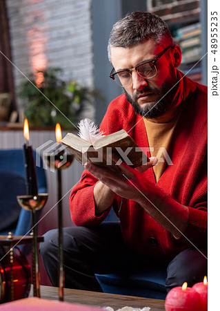 Fortune-teller reading astrology book sitting at the table with candles 48955235